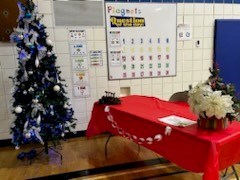Table set up for ticket sales with a white poinsettia on right side.. There is a Christmas tree set up beside it.