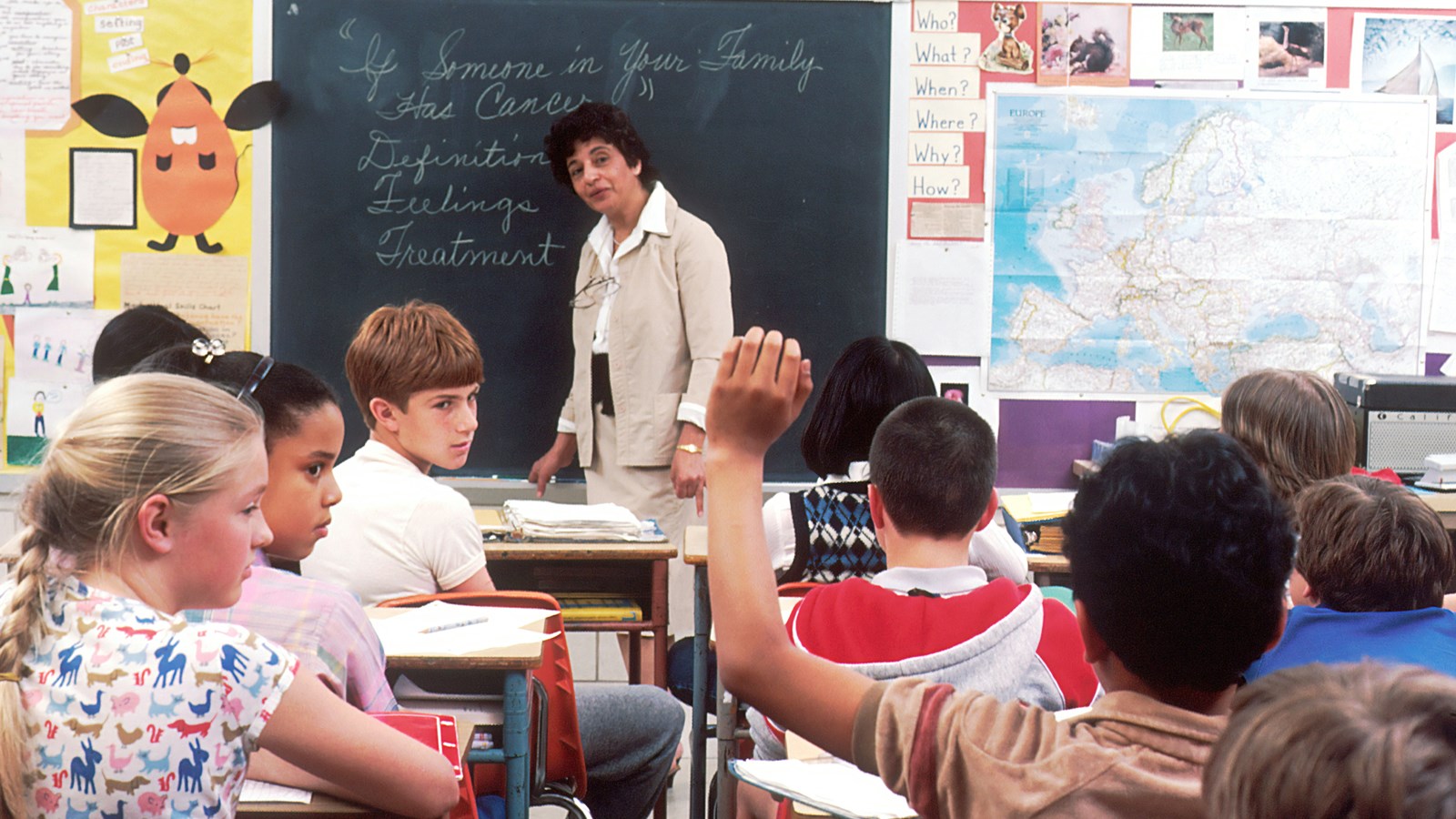 Students sitting in desks with a female teacher at the front of a classroom